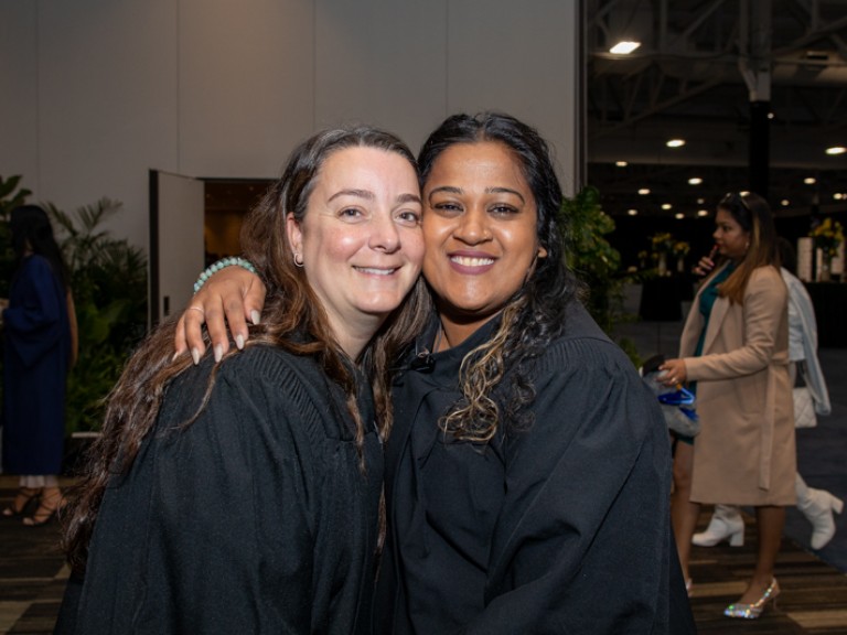Two people in black robes smile for photo