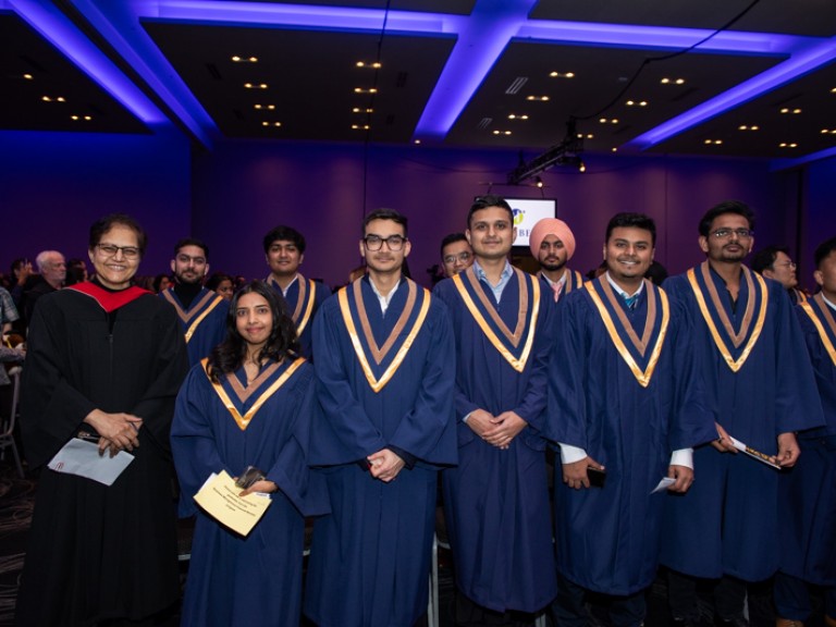 Graduates standing in ceremony hall look at camera