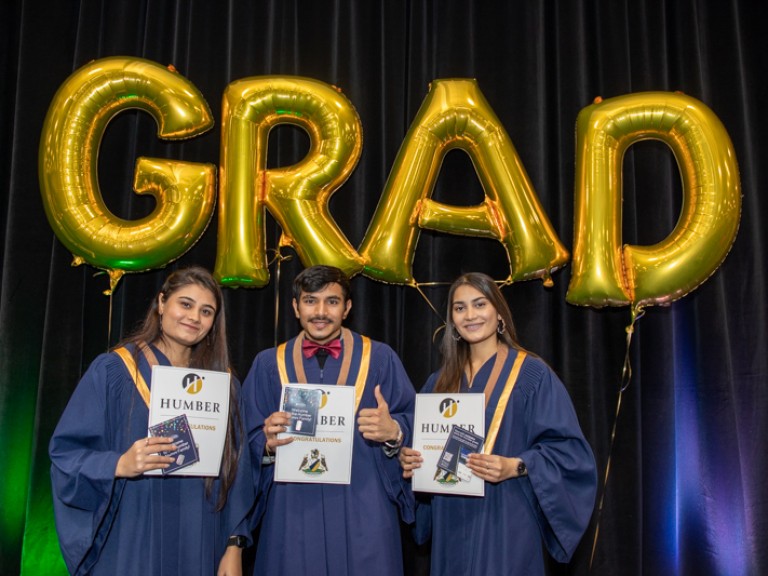 Three graduates take photo in front of GRAD balloons