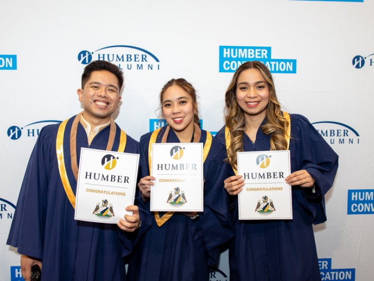 Three graduates holding their certificates smile for photo