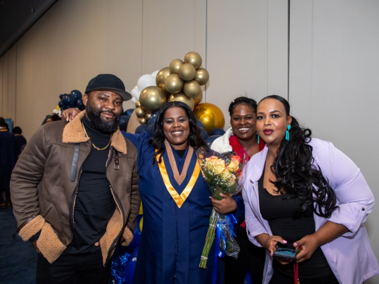 Graduate takes photo with three guests in front of balloons