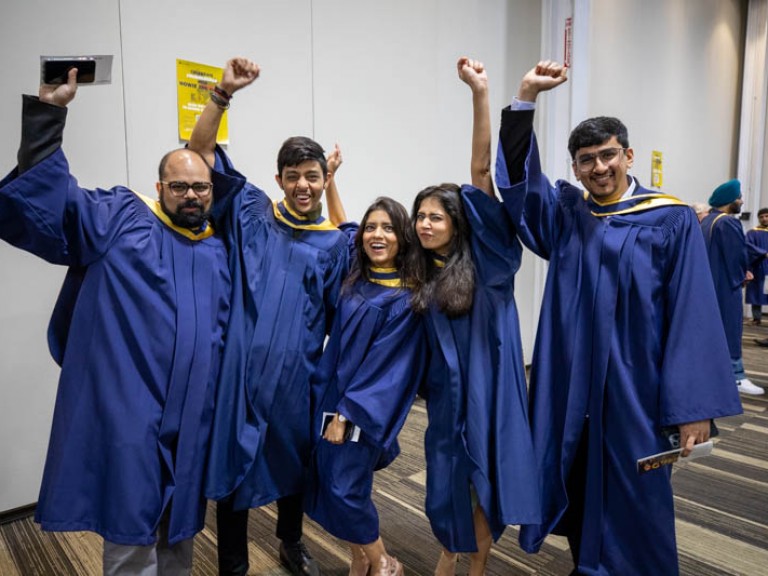 Five graduates raising their arms in celebration