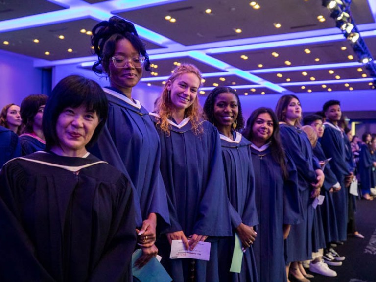 Line of graduates in front of their seats smiling for camera