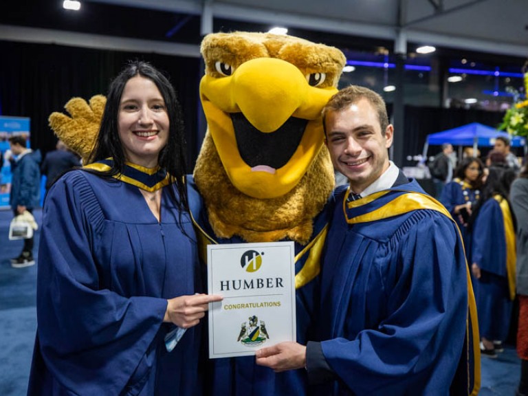 Two graduates taking photo with Humber mascot