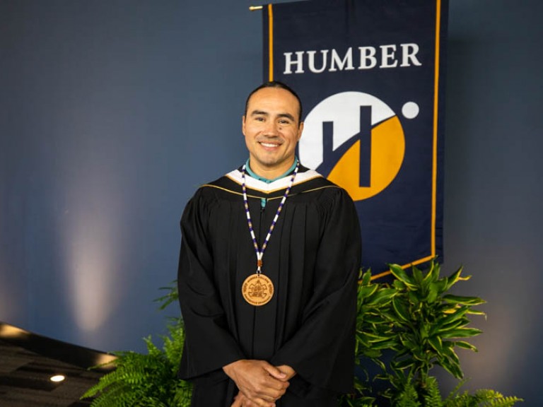 Honorary degree recipient Michael Linklater standing in front of Humber flag