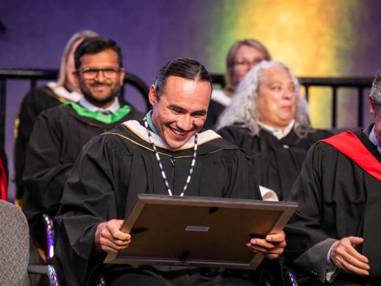 Michael Linklater seated and smiling at his degree
