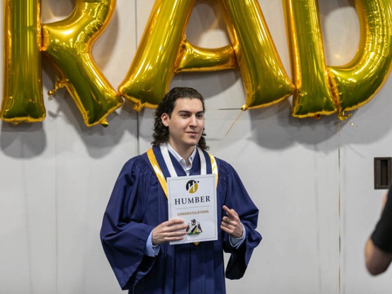 Graduate posing for photo in front of GRAD balloons