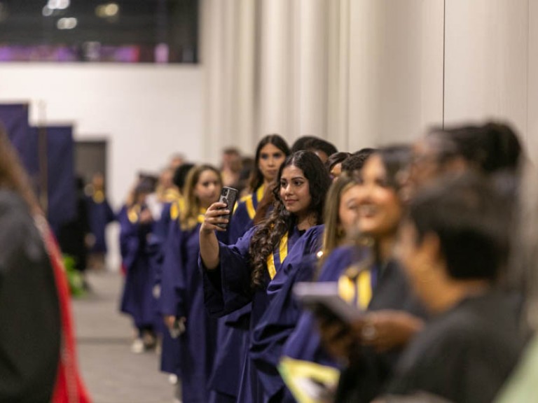 A graduate in line takes a photo with her phone