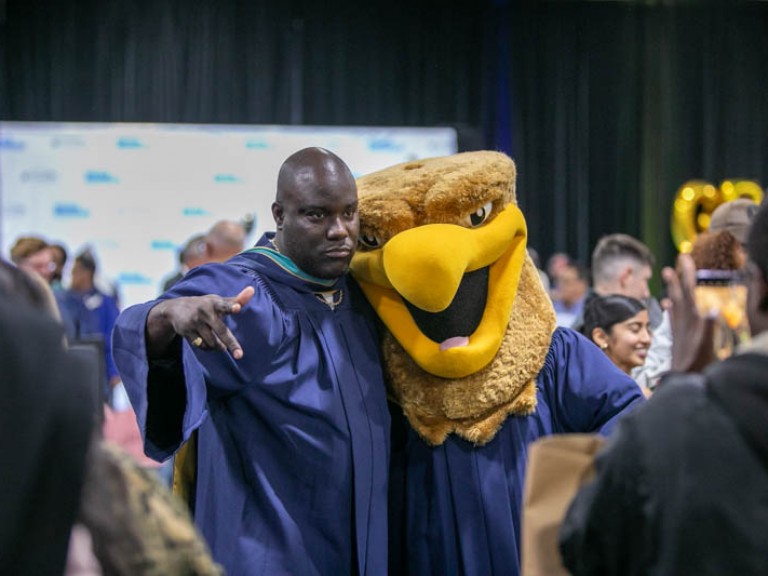 Graduate posing for photo with Humber mascot