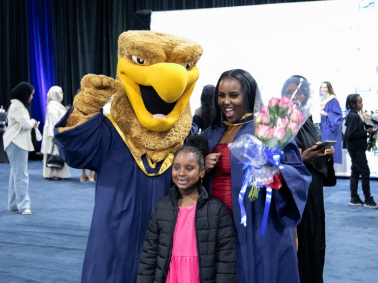 Graduate posing for photo with child and Humber mascot