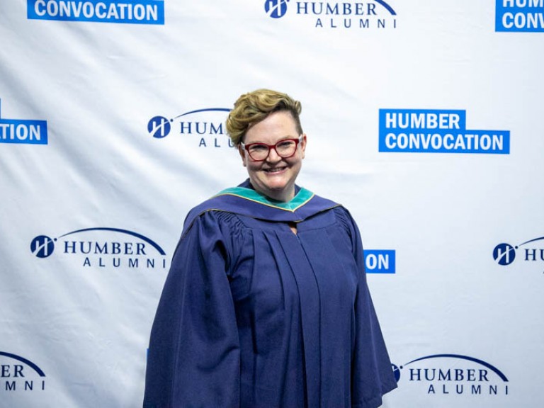 Graduate smiling for photo in front of Humber Convocation wall
