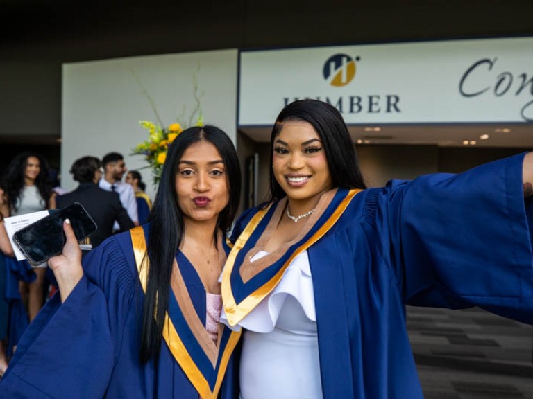 Two graduates posing for photo together with arms up