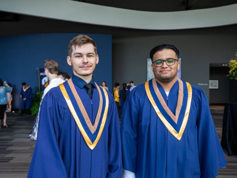 Two graduates in gowns posing for photo