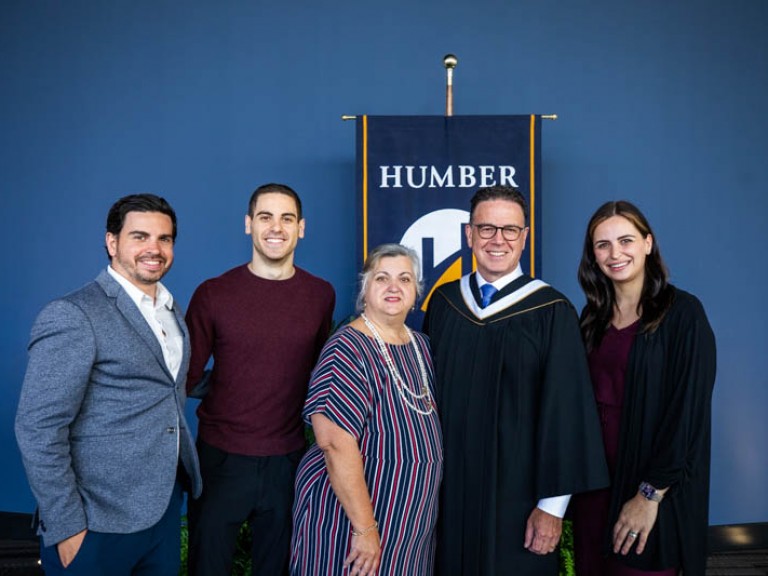 Five people pose for photo in front of Humber flag, including honorary degree recipient