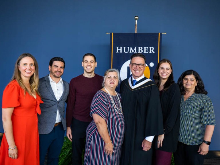 Seven people pose for photo in front of Humber flag, including Anthony Longo