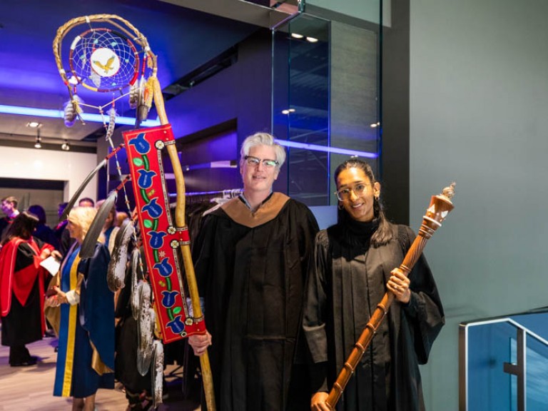 Two faculty members holding Indigenous staffs outside faculty dressing area