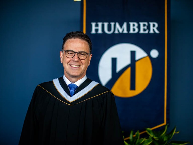 Honorary degree recipient Anthony Longo smiles for photo in front of Humber flag