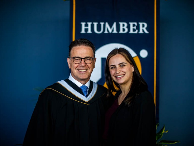 Anthony Longo and ceremony guest pose for photo in front of Humber flag