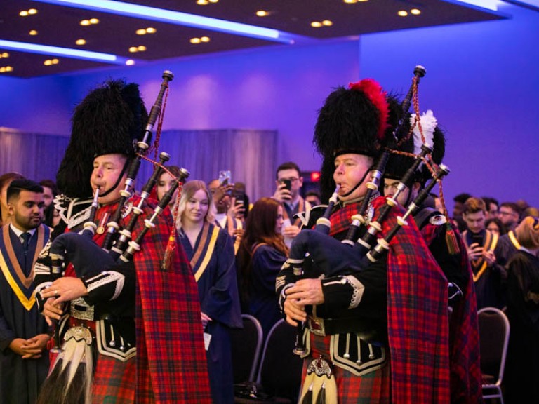 Musicians in Scottish regalia playing bagpipes in ceremony hall