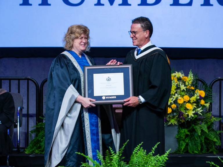 Honorary degree recipient Anthony Longo and Humber president Ann Marie Vaughan holding framed degree between them on stage