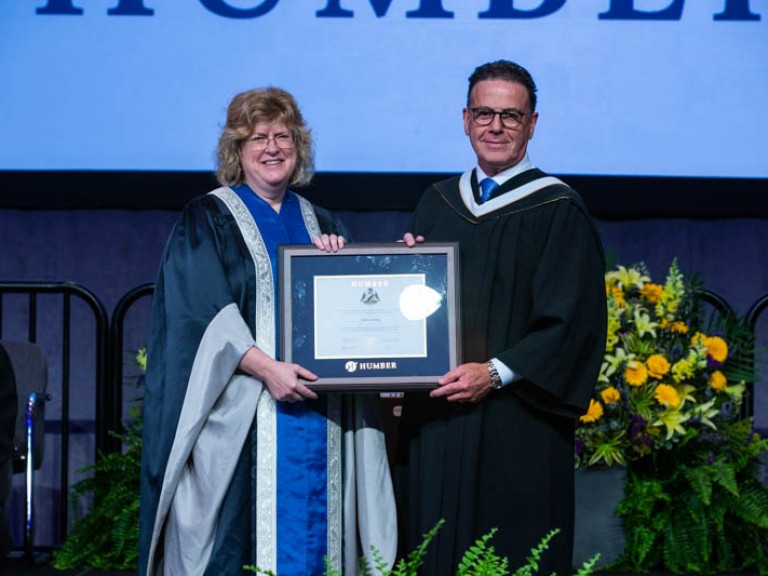 Honorary degree recipient Anthony Longo and Humber president Ann Marie Vaughan holding framed degree between them on stage