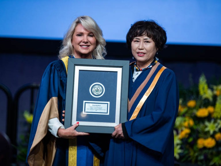 Two people on stage holding framed award between them and pose for photo