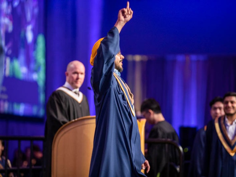 Graduate on stage pointing up in celebration