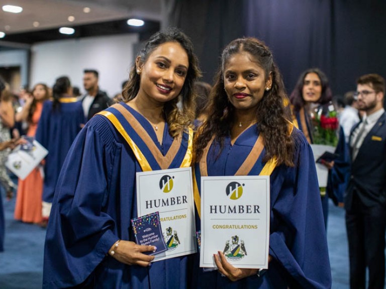 Two graduates in reception area holding certificates posing for photo