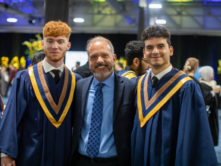 Two graduates with ceremony guest between them pose for photo