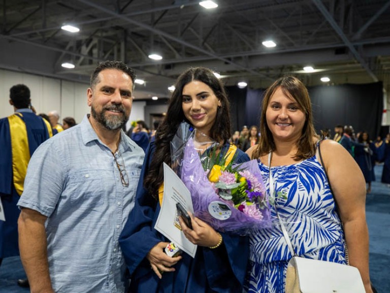 Graduate holding flowers posing for photo with parents
