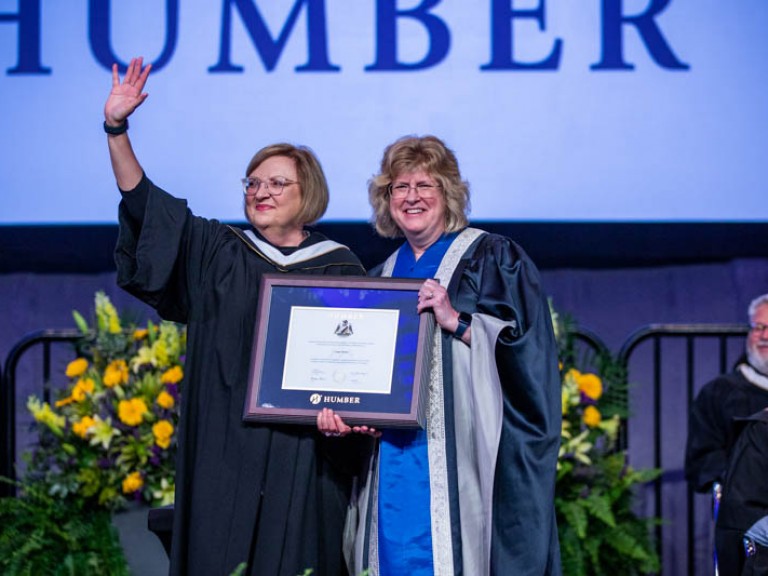 Lana Payne waves as she holds her framed degree with Ann Marie Vaughan on stage