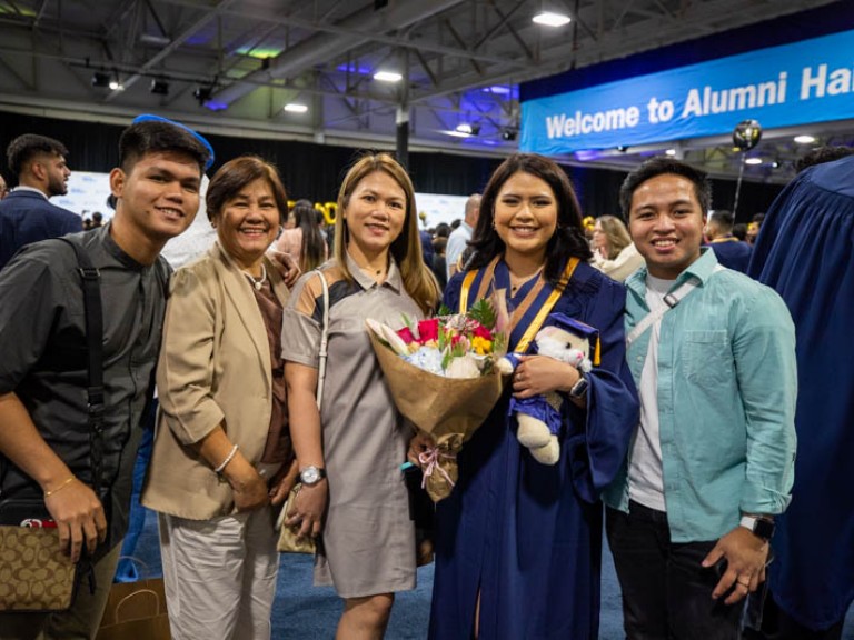 Graduate holding flowers and teddy bear takes photo with family