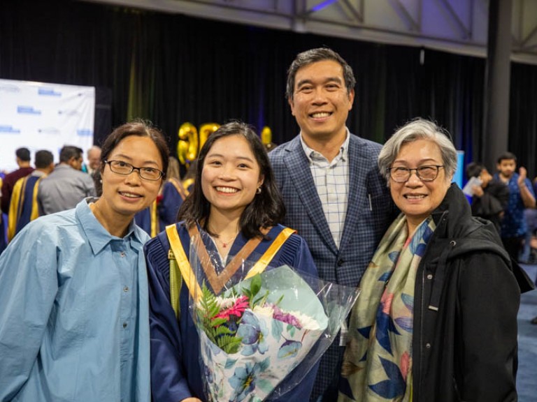 Graduate holding flowers poses for photo with three family members