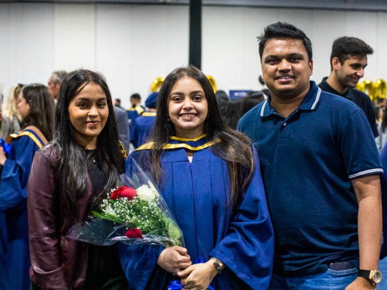 Graduate holding flowers poses for photo with two guests