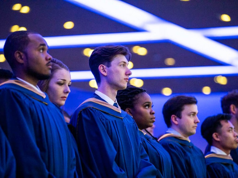 Row of graduates standing looking towards stage