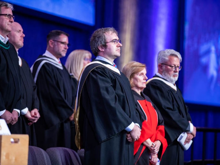 Honorary degree recipient Andrew Monkhouse standing with faculty on stage