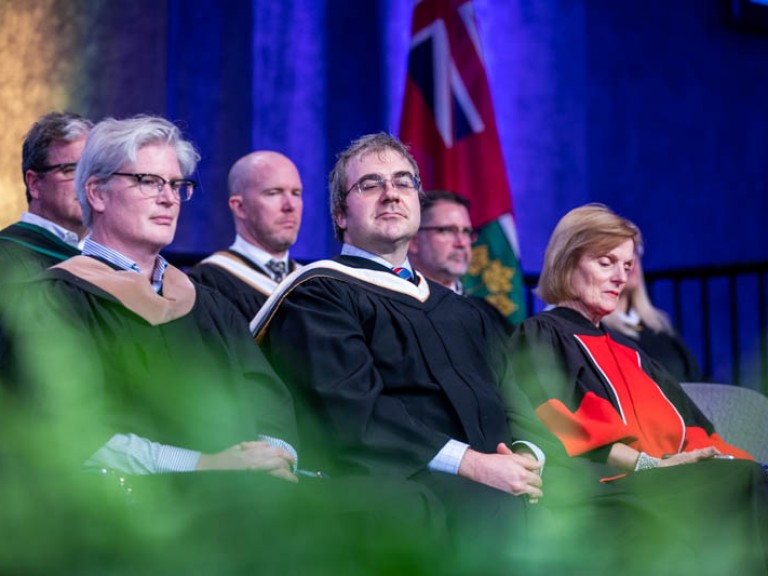 Andrew Monkhouse sitting between faculty members on stage