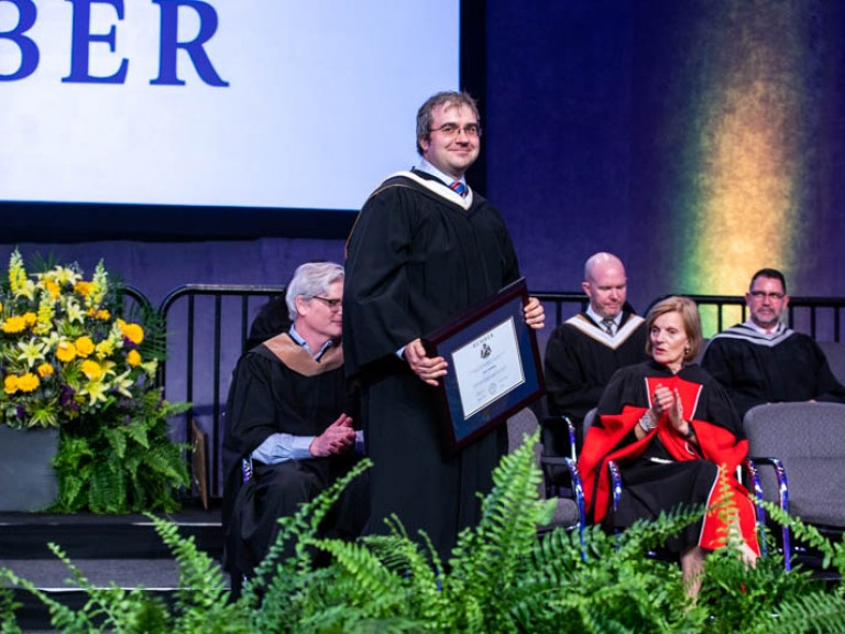 Andrew Monkhouse returning to his seat with framed degree