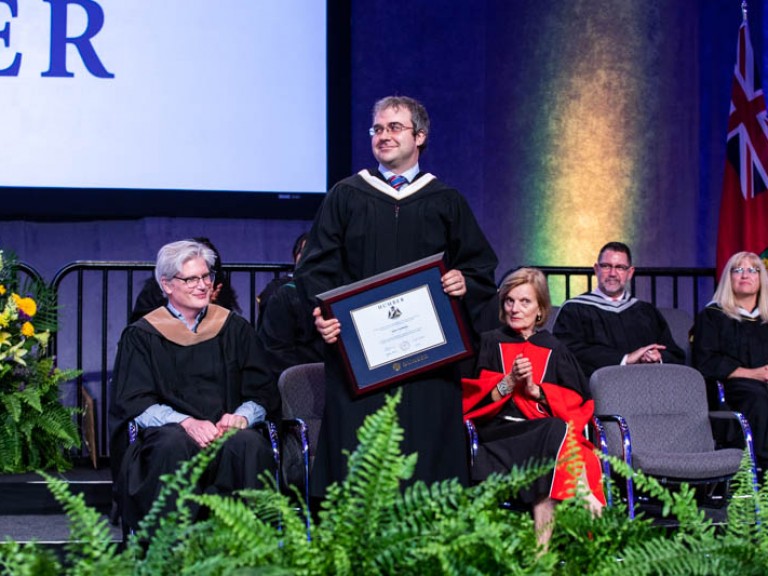 Andrew Monkhouse standing on stage with framed degree