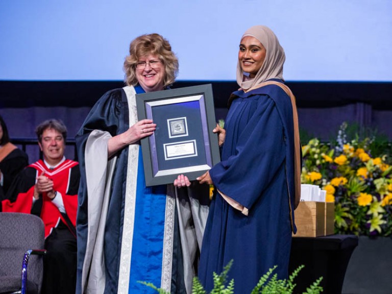 Graduate and Ann Marie hold framed award as they smile for camera