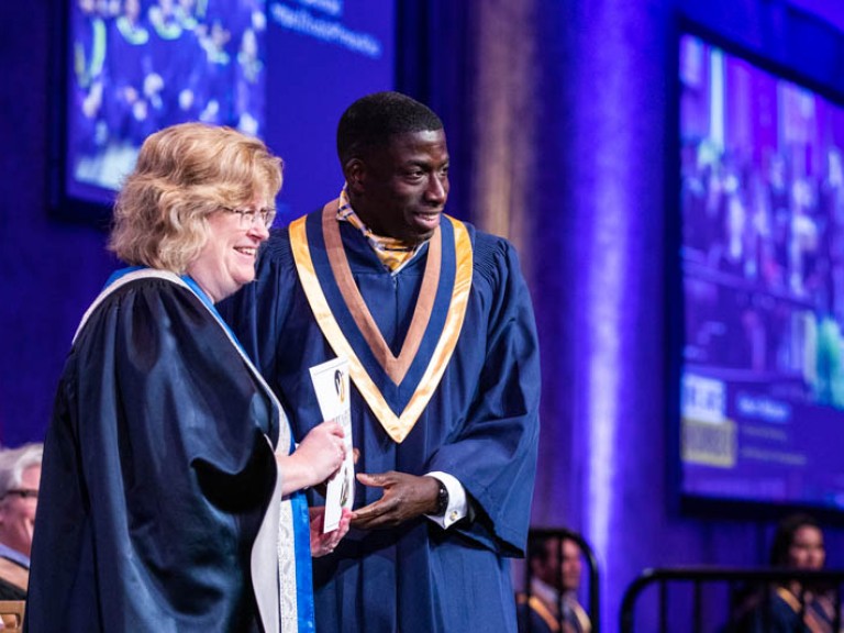 Graduate posing for photo with Ann Marie Vaughan on stage