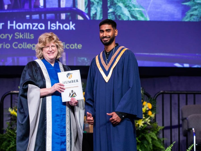 Graduate making thumbs up beside Ann Marie on stage