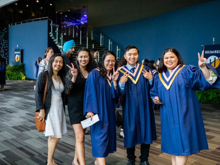 Three graduates holding up peace signs for photo beside two ceremony guests