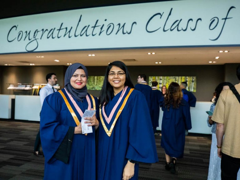 Two graduates posing for photo in reception hall