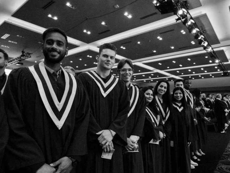 Black and white photo of graduates standing in audience