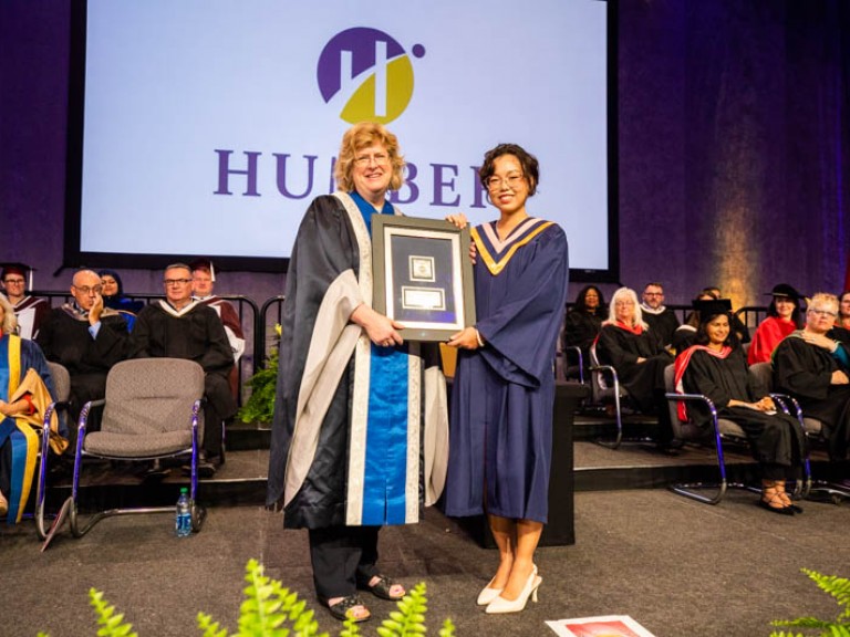 Graduate holding framed award with Ann Marie Vaughan on stage