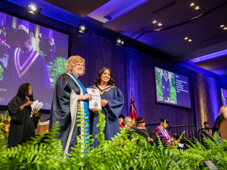 Graduate on stage holding congratulations paper with Ann Marie