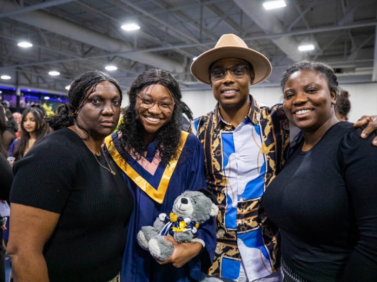 Graduate holding teddy bear takes photo with three family members