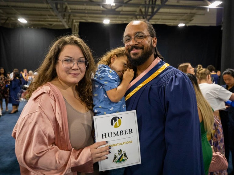 Graduate holding toddler takes photo with ceremony guest