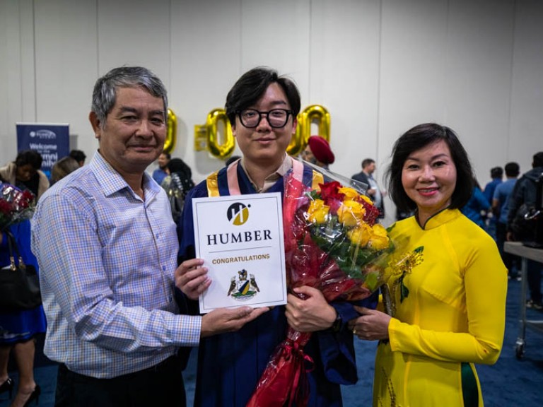 Graduate holding flowers takes photo with parents